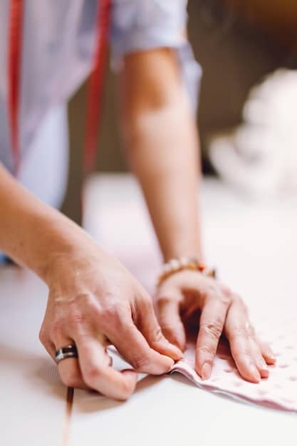 A close-up shot of a young French designer's hands meticulously working on a complex garment construction. The designer is surrounded by various tools and materials, highlighting the craftsmanship and attention to detail involved in the fashion creation process.
