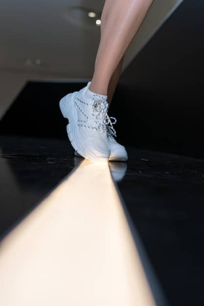 A pair of futuristic silver sneakers with glowing accents, placed on a minimalist white platform. The sneakers showcase innovative design with geometric shapes and a sleek, aerodynamic silhouette, representing the cutting-edge footwear trends of 2025.