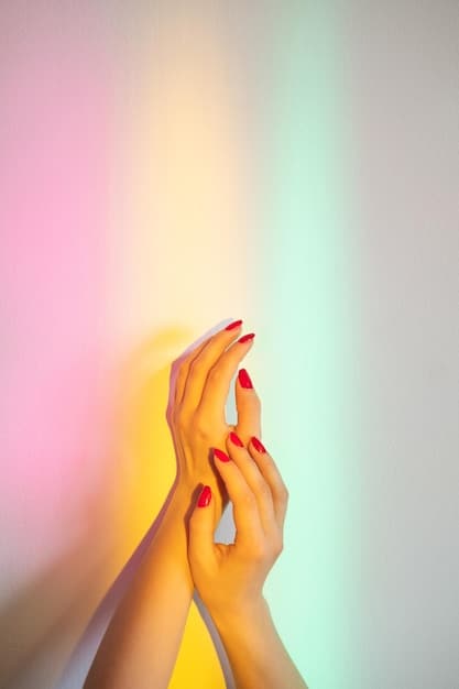 An eye-level shot of a woman's hands with brightly colored neon nail polish. The nails are different shades, including lime green, hot pink, and electric blue. The background is a blurred outdoor setting with natural light.