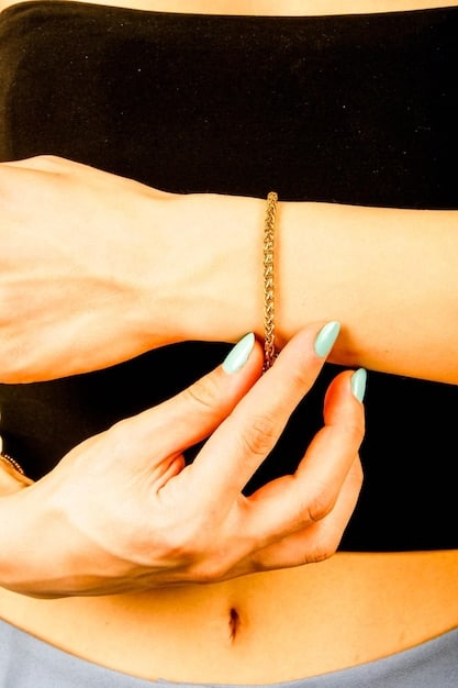 A close-up shot of a woman's hands, showcasing delicate gold rings and a simple gold bracelet. The background is blurred, focusing on the jewelry.