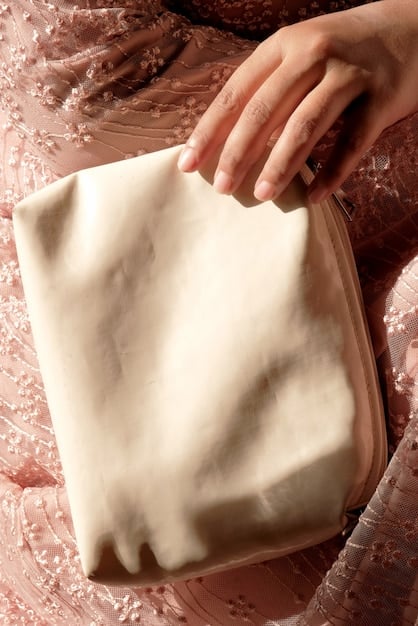 A close-up of a stylish woman's hands tying a silk scarf around the handle of a structured leather tote bag. The scarf has a classic pattern, and the bag is a neutral color.