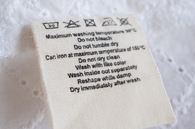 A close-up of a garment care label, clearly showing various symbols for washing, drying, ironing, and bleaching instructions. The background is a soft, blurred image of a clothing rack.