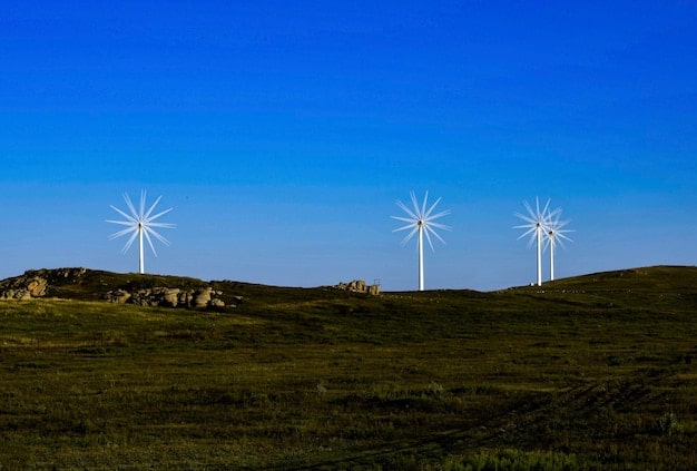A detailed close-up shot of wind turbines on a wind farm in Alberta, Canada, set against a twilight sky. The windmills should be silhouetted with their blades rotating, symbolizing the generation of clean electricity. The image emphasizes the height and scale of the turbines, and the golden hour lighting should give the photo a warming effect, creating a mood of calm industry and sustainable progress.