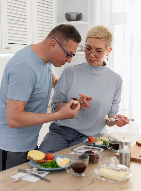 An occupational therapist is demonstrating adaptive equipment to an elderly man in his kitchen, helping him maintain independence in meal preparation.