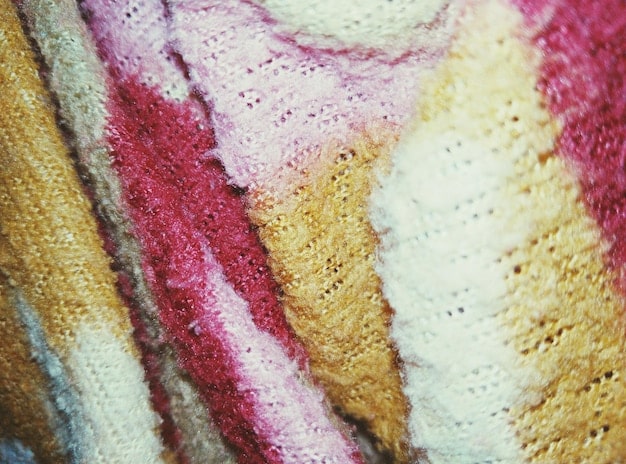 A close-up shot of a variety of knitted sweaters in different textures and colors, including chunky cable knits, fine-gauge merino wool, and colorful patterned sweaters. The sweaters are neatly arranged on a wooden shelf.