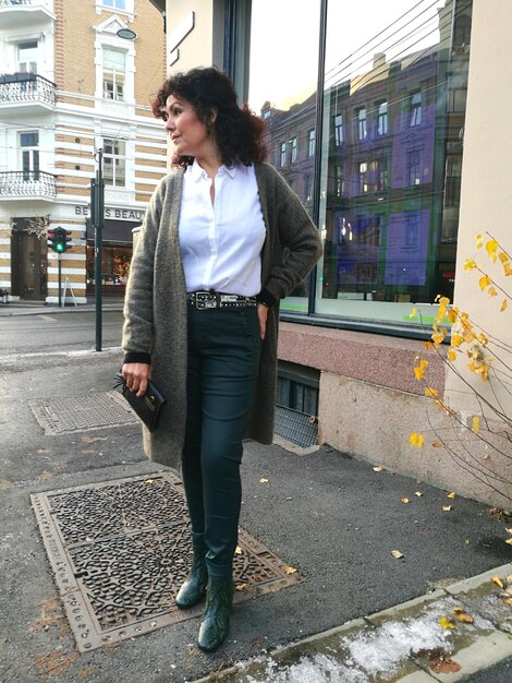 A woman wearing a smart casual outfit consisting of a button-down shirt, a cardigan, and dark wash jeans. She is accessorized with a crossbody bag and ankle boots.