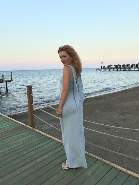 A woman in a flowing sundress made of Tencel or Lyocell, standing on a sunny beach, wearing sunglasses and holding a reusable tote bag. The dress is light and airy, symbolizing sustainable summer fashion.