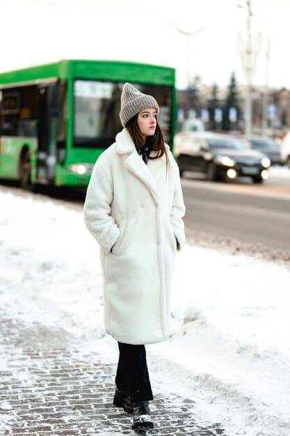 A person wearing a stylish winter coat made from recycled materials, standing in a snowy cityscape. The coat is paired with a hat and gloves made from sustainable wool.