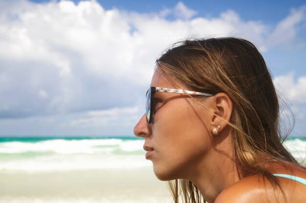 A close-up of a woman with sun-kissed skin, shimmery highlighter on her cheekbones, and loose, beachy waves in her hair. She is wearing a stylish sun hat and sunglasses.