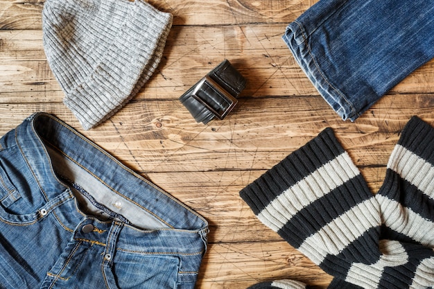 A close-up shot of various layering essentials, including a lightweight thermal top, a denim jacket, a cardigan, and a scarf, neatly arranged on a wooden surface.