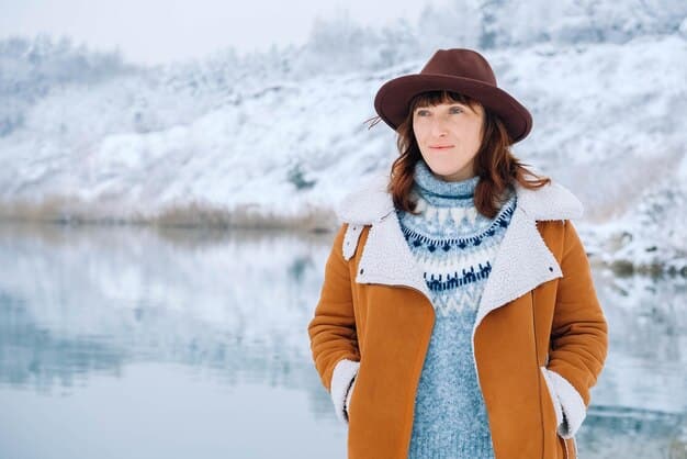 A person dressed in a winter layered outfit, featuring a thick wool coat, a scarf, gloves, and a hat, standing in a snowy landscape.