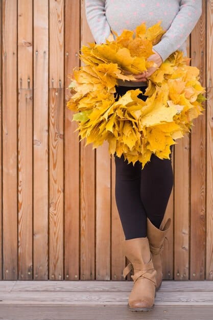 An image showing a person wearing completely mismatched accessories for autumn - bright summer-colored sandals with a heavy fall coat and scarf. The background is an autumn scene with falling leaves.