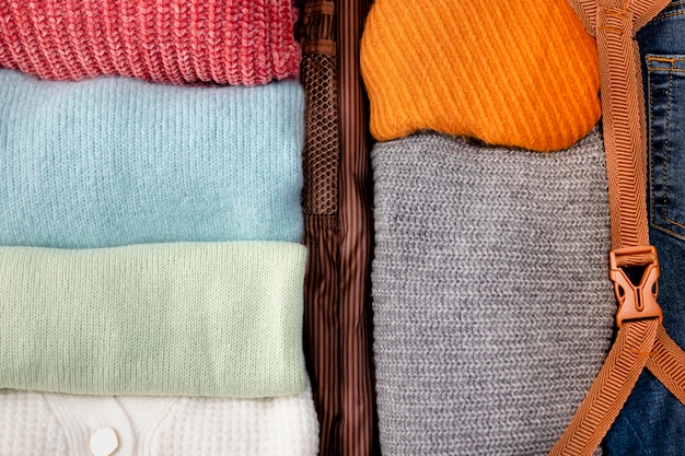 Close-up shot of a neatly organized section of a capsule wardrobe. It features folded sweaters in neutral colors, a stack of crisp white shirts, and a pair of dark wash jeans. The arrangement highlights the minimalist aesthetic and the emphasis on timeless, versatile pieces.