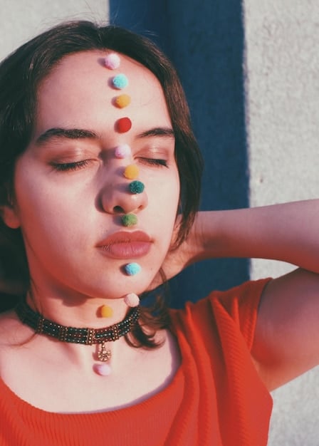 A close-up shot of a model wearing a large, colorful beaded necklace and oversized geometric earrings from Shein. The background is a blurred, vibrant cityscape.