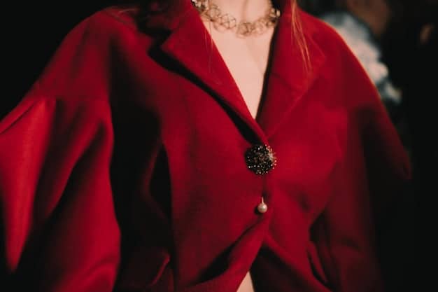 A close-up of a woman wearing a ruby red velvet dress with delicate gold jewelry, showcasing its texture and elegance.