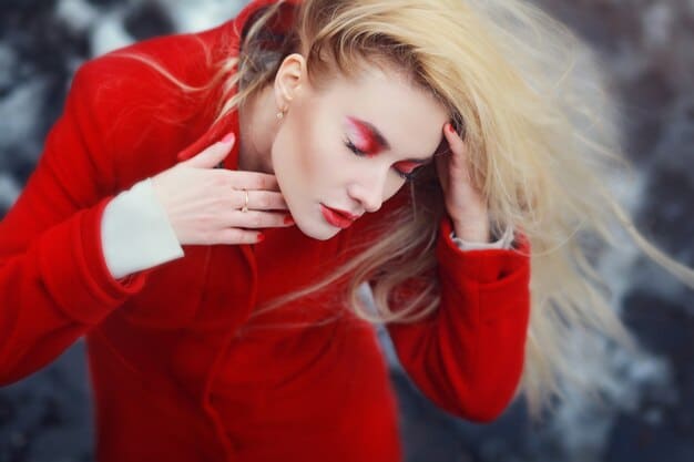 A woman with glamorous holiday makeup featuring a bold red lip, shimmery eyeshadow, and perfectly styled waves in her hair.